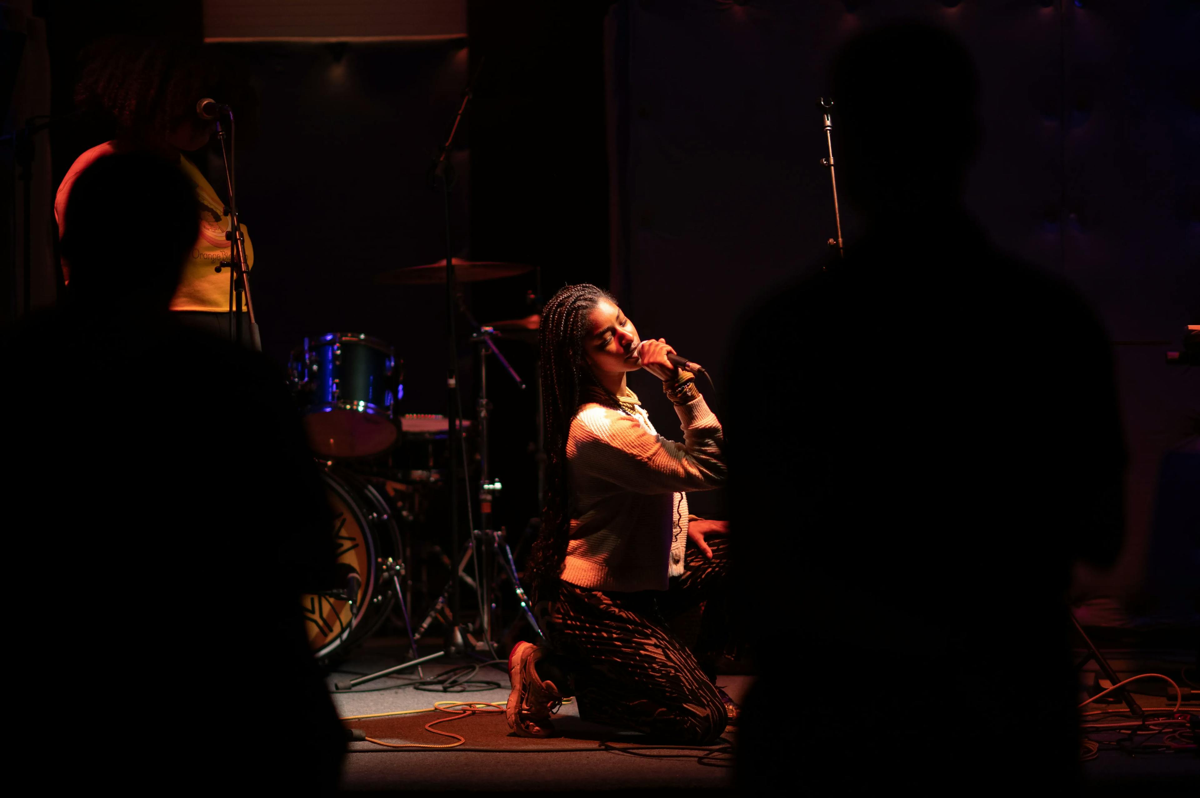 Woman kneeling on a stage singing to a crowd at The Pocket in Washington DC.